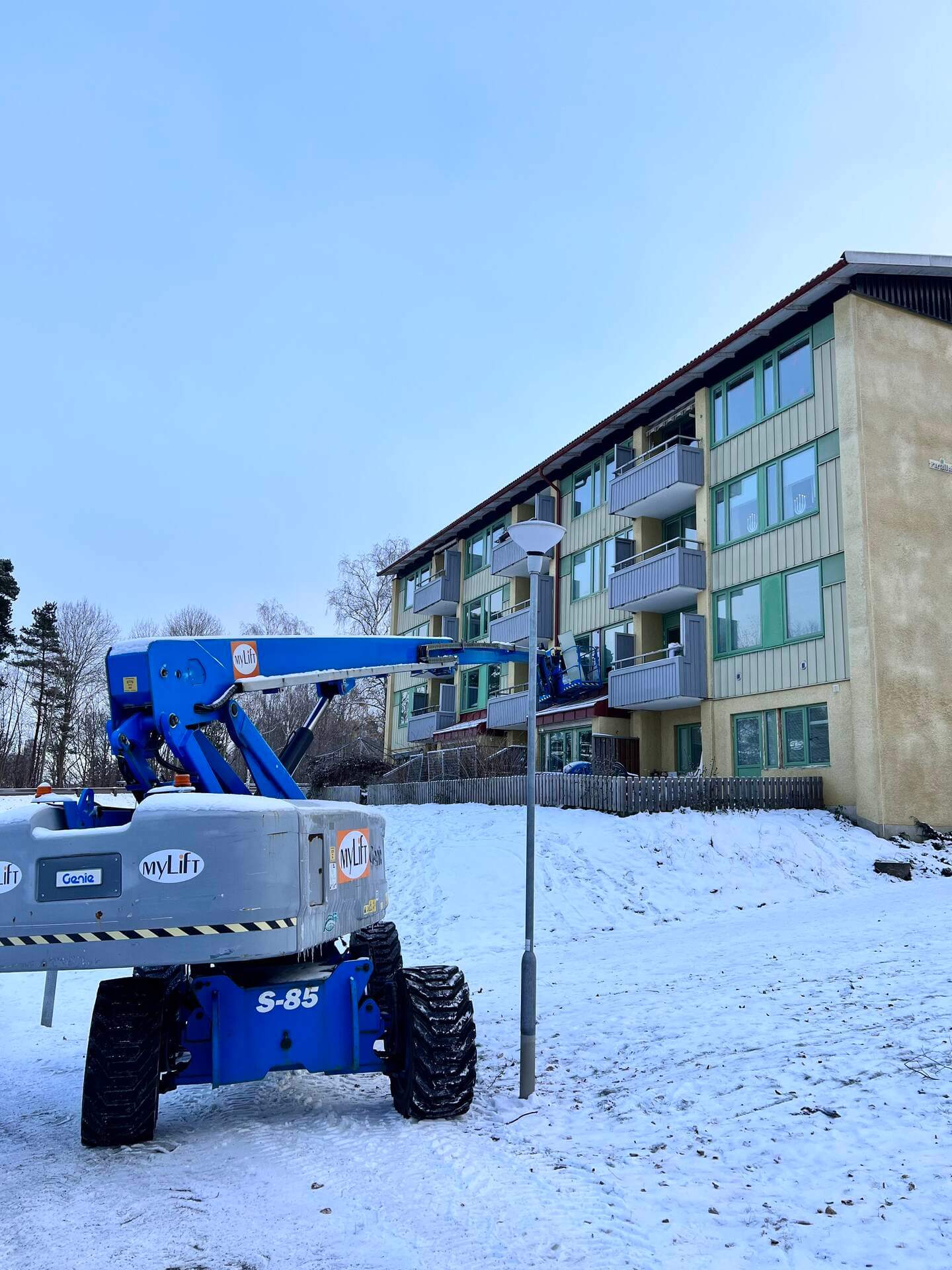 Skylift uppställd vid flerbostadshus under pågående fönsterbyte i vinterväglag