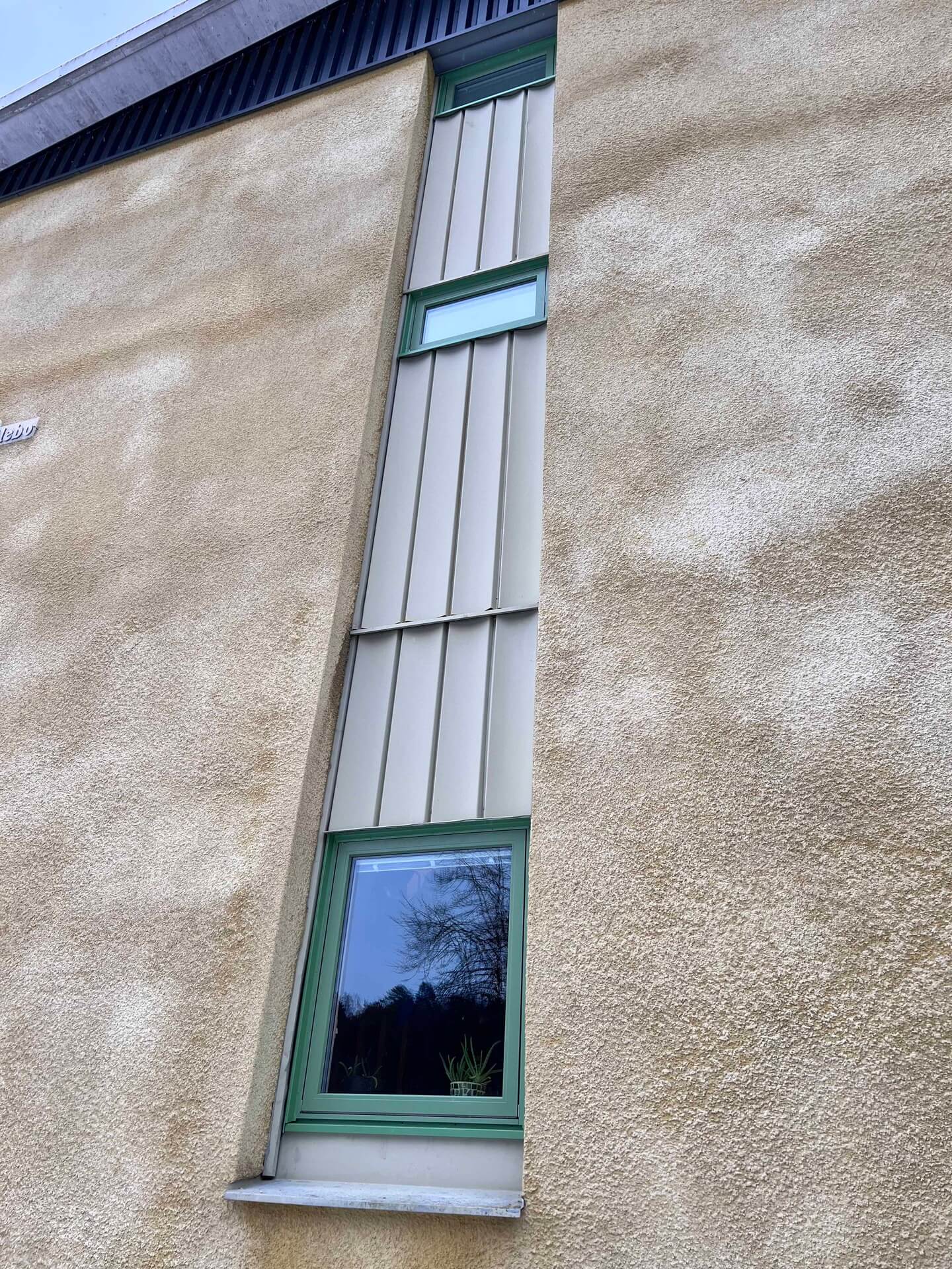 Närbild på grön fönsterprofil monterad mot putsad fasad