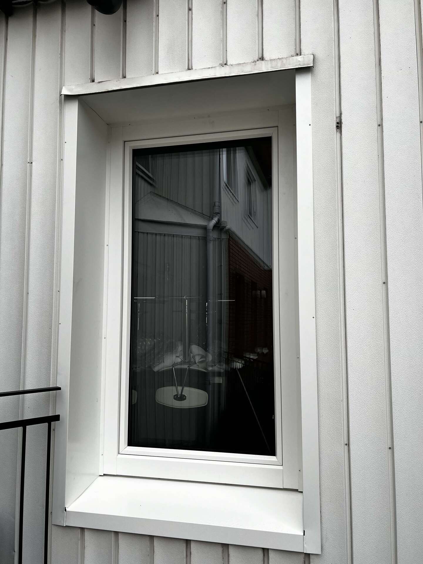 Fönster med vit karm och smalt sidoljus på vit vertikal träpanelfasad