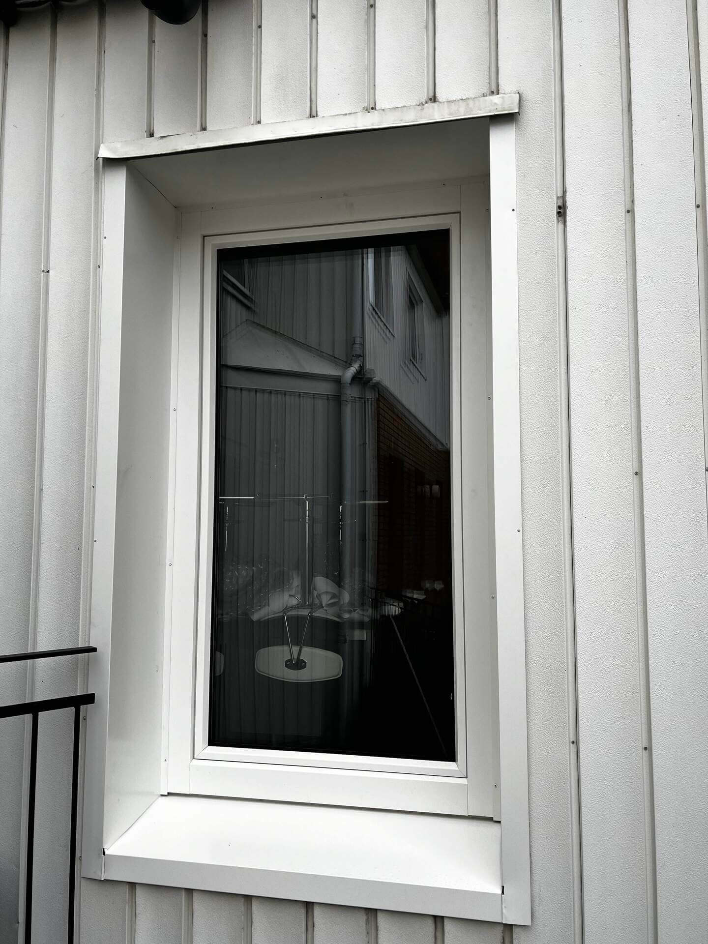 Närbild på fönster med vit karm monterad i vit träpanelfasad