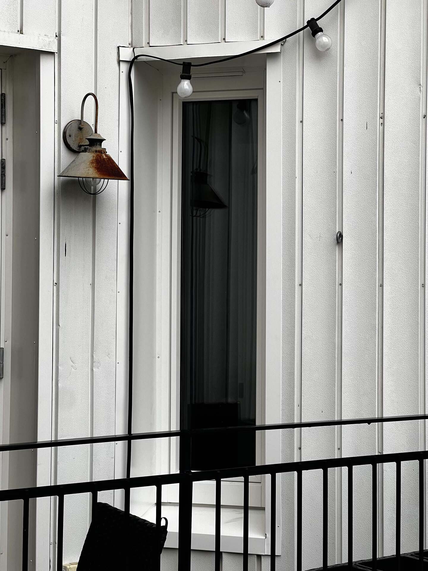 Nyinstallerat fönster med smalt sidoljus på vit träpanelfasad med industrilampa
