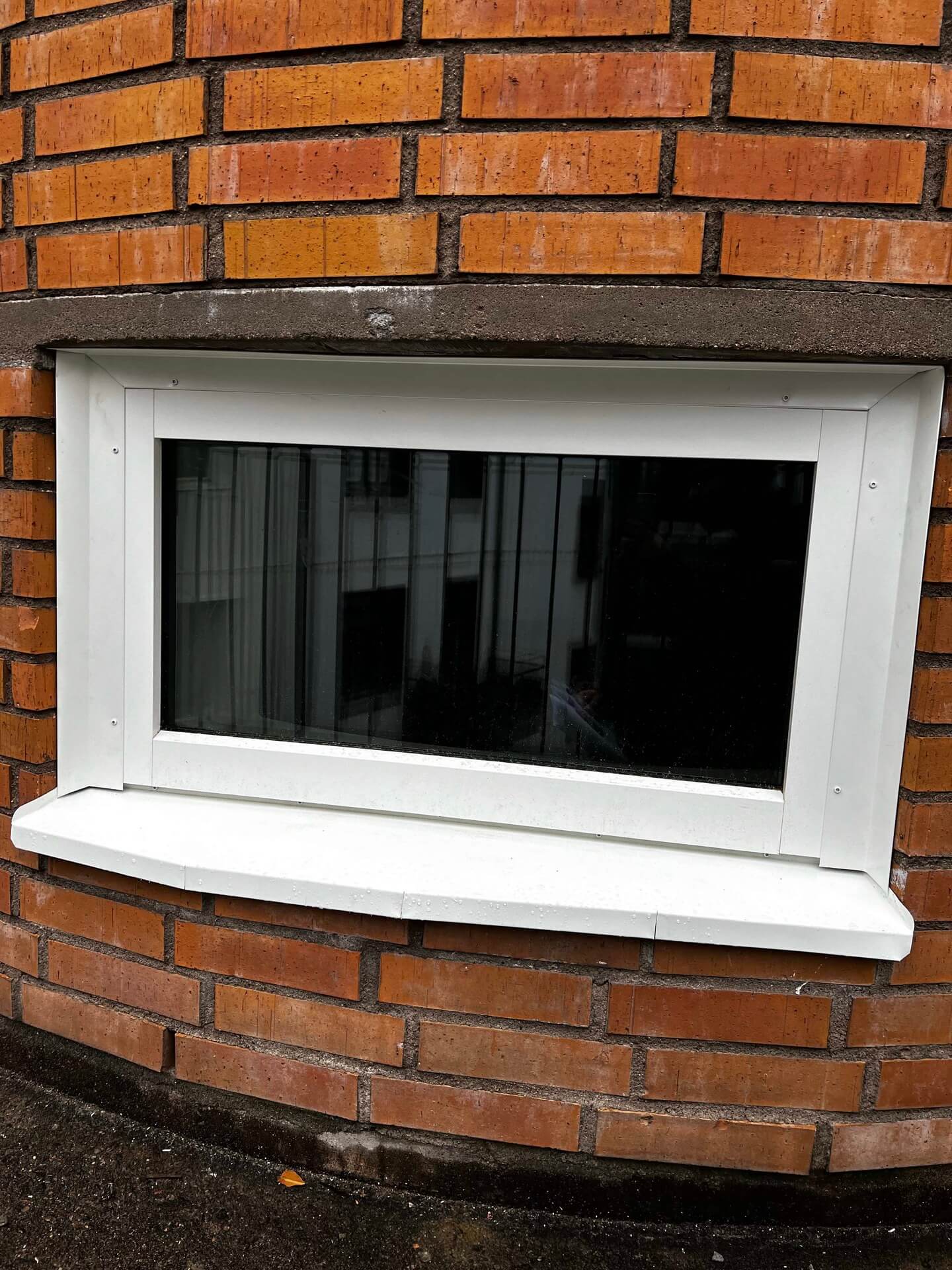 Nyinstallerat liggande fönster med vit karm och bred fönsterbänk i tegelfasad