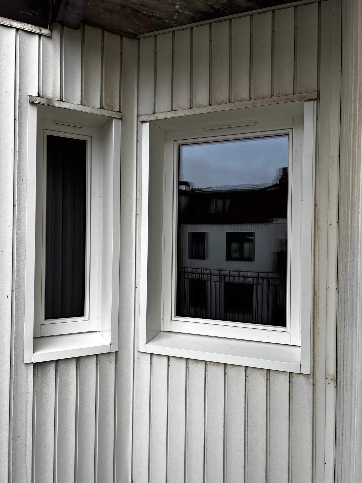 Nyinstallerade höga fönster med vita karmar och foder på vit träpanelfasad