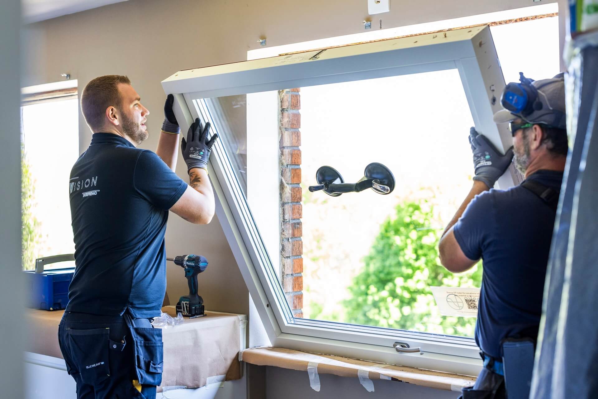 Två montörer från Vision Entreprenad lyfter in fönsterbåge med suglyft i tegelfasad