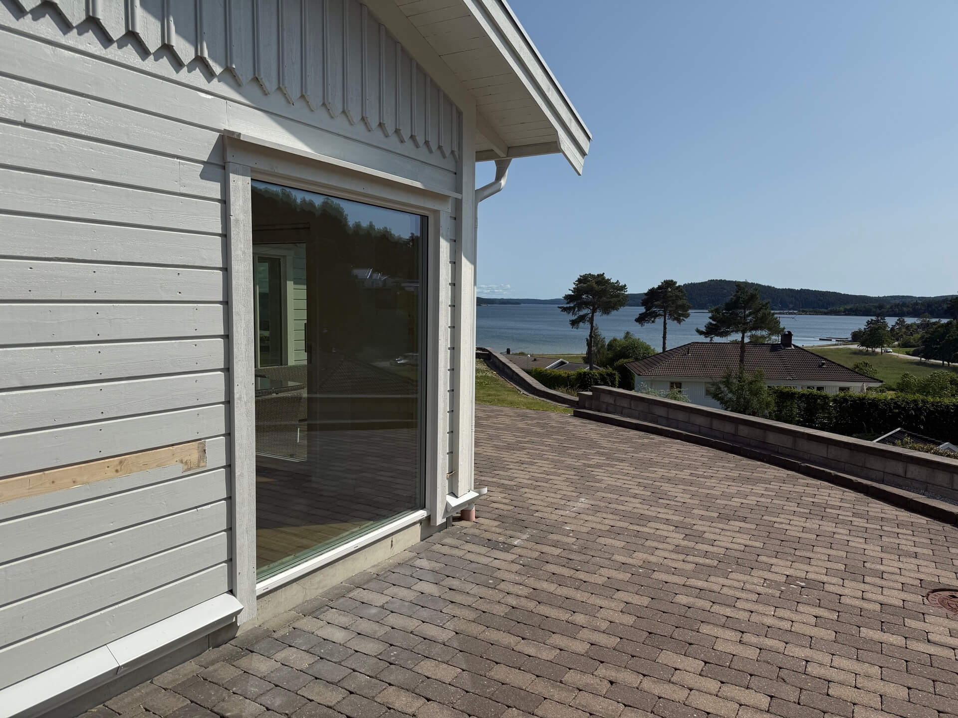 Brett skjutparti på grå villa mot stensatt altan med havsutsikt