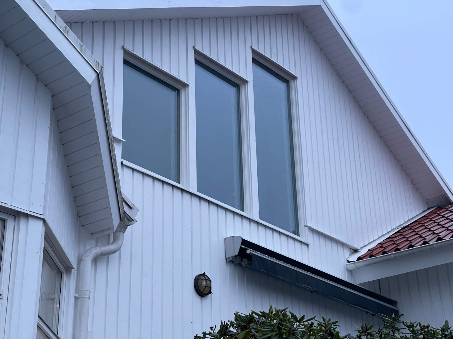 Närbild på tre nyinstallerade fönster i gavelspets på vit träpanelfasad