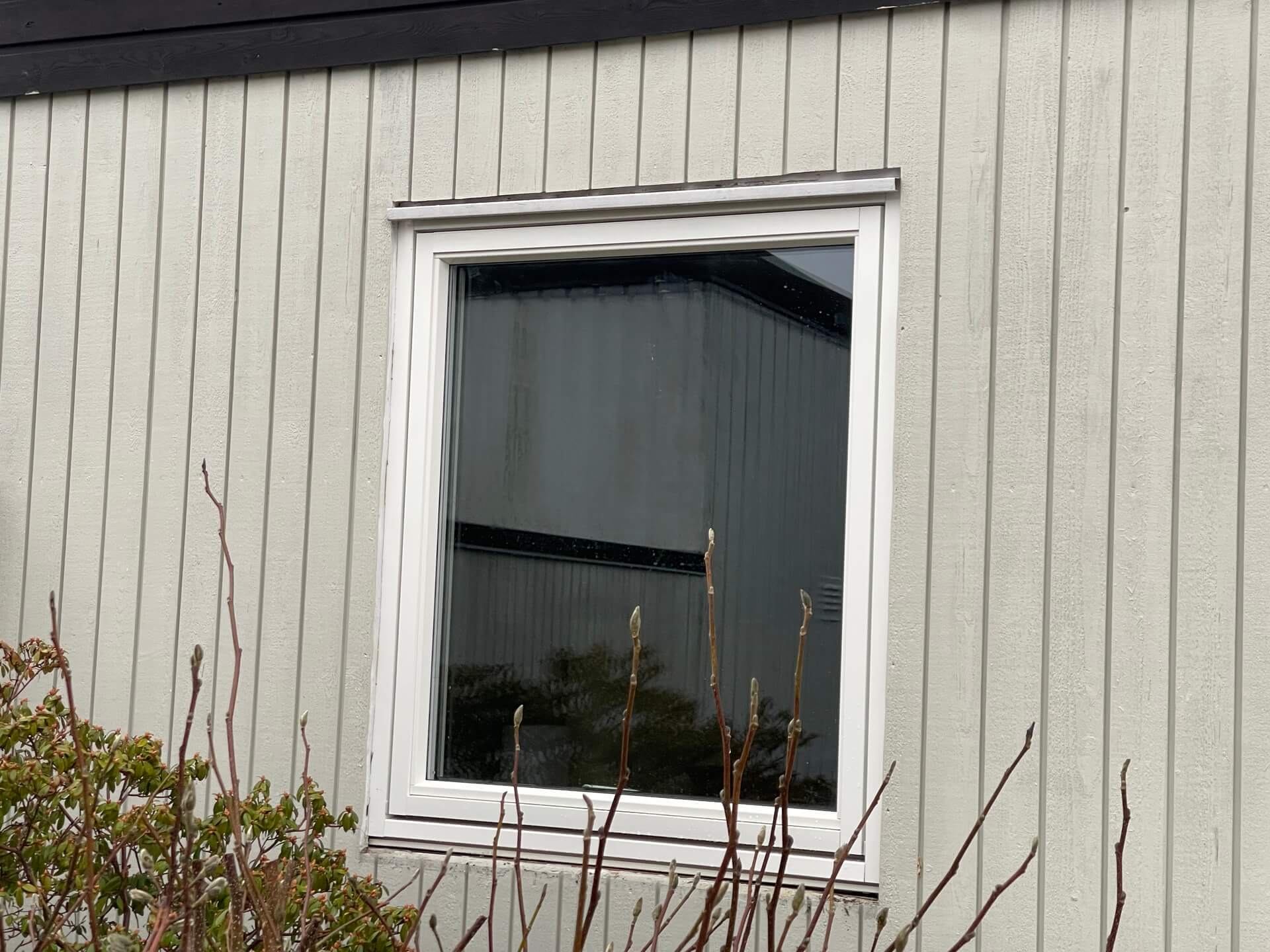Nyinstallerat fönster med vit karm och underbleck på grå vertikal träpanelfasad