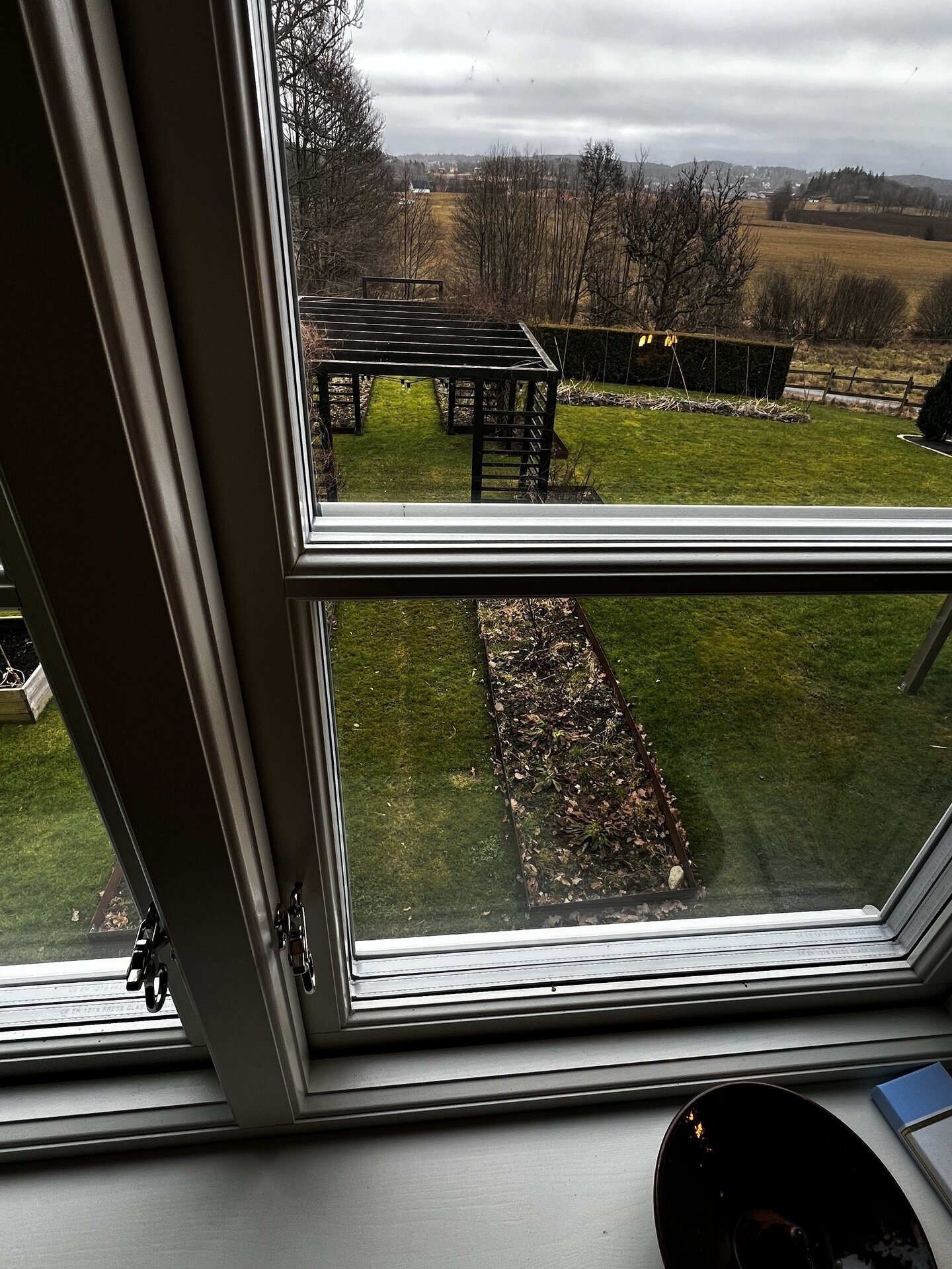 Närbild på öppnat fönster med mörk karm och utsikt över trädgård
