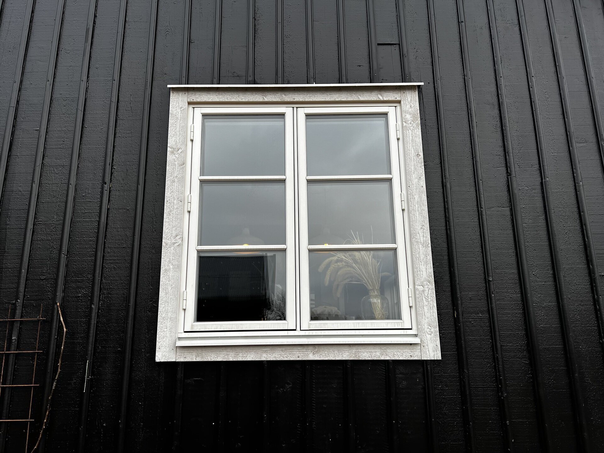 Närbild på nyinstallerat tvåluftsfönster med vit karm på svart träpanelfasad