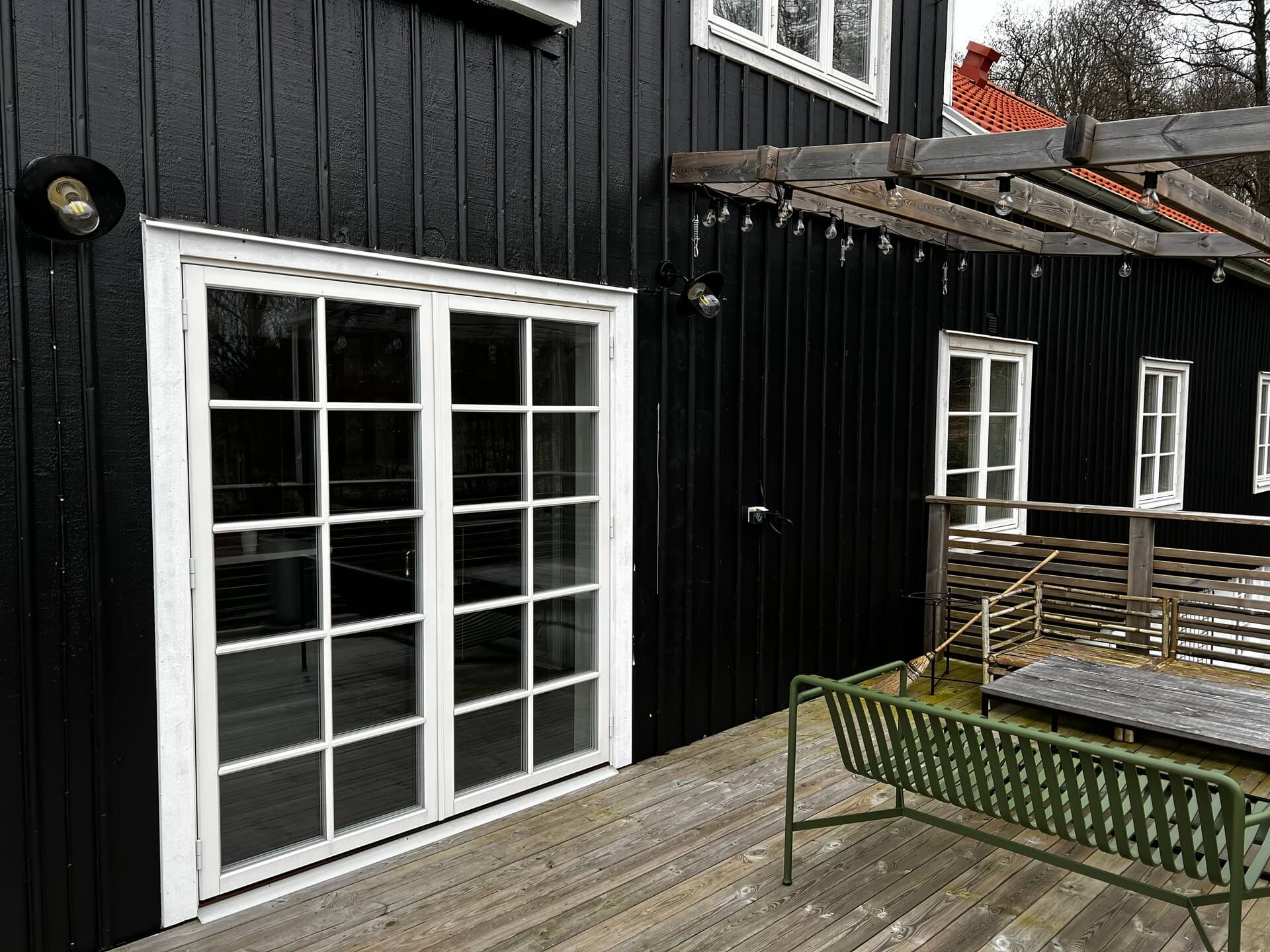 Närbild på vita spröjsade pardörrar mot trädäck på svart träpanelfasad