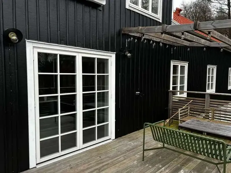Närbild på vita spröjsade pardörrar mot trädäck på svart träpanelfasad – utfört av Vision Entreprenad