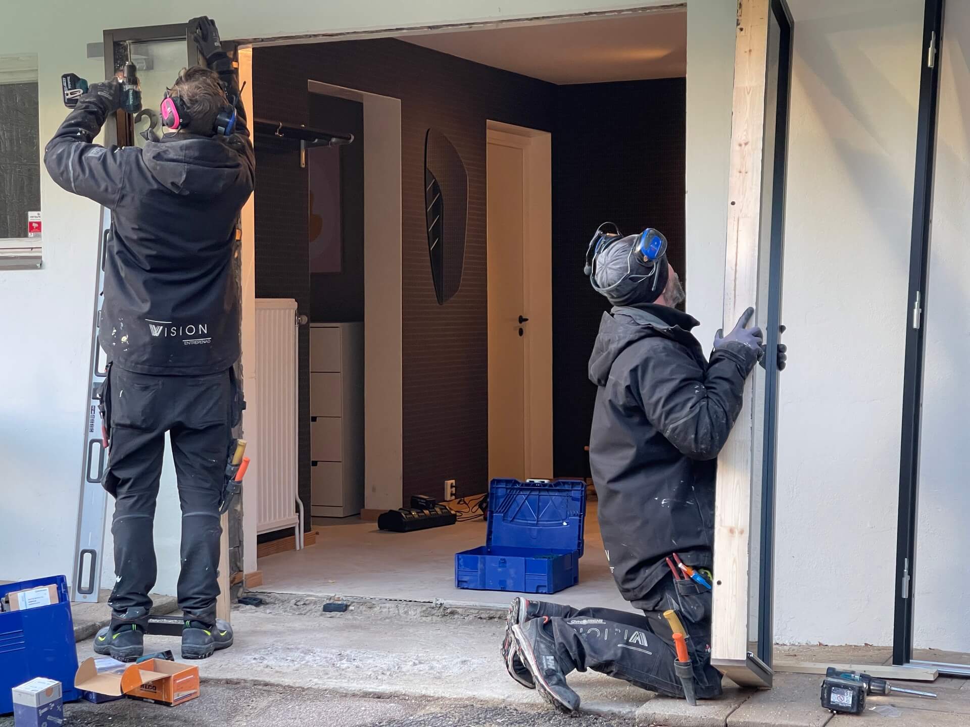 Två montörer från Vision Entreprenad installerar ny ytterdörr i dörrkarmen