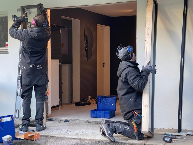 Två montörer från Vision Entreprenad installerar ny ytterdörr i dörrkarmen