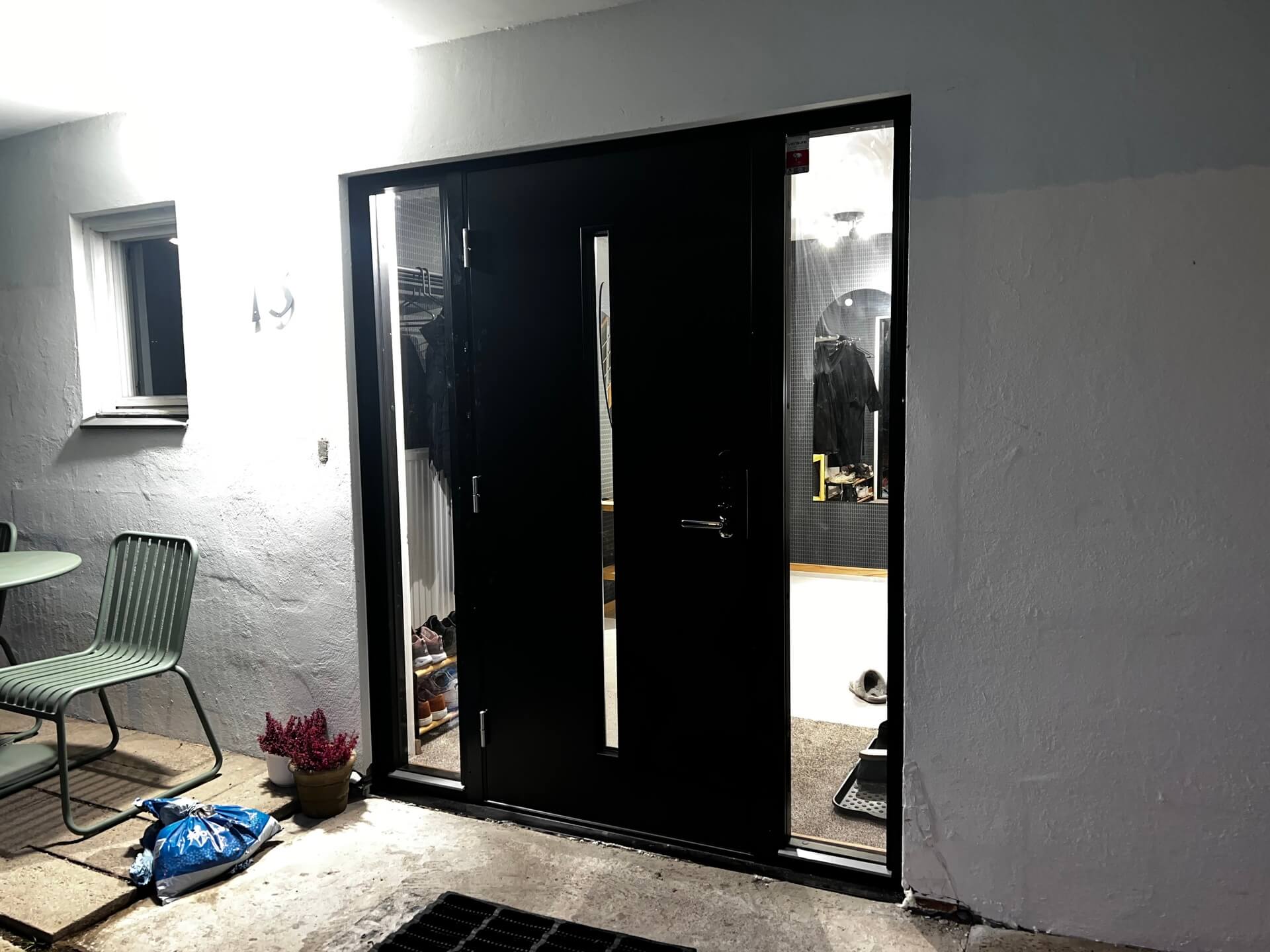 Nyinstallerad svart ytterdörr med smalt sidoljus öppnad mot entré