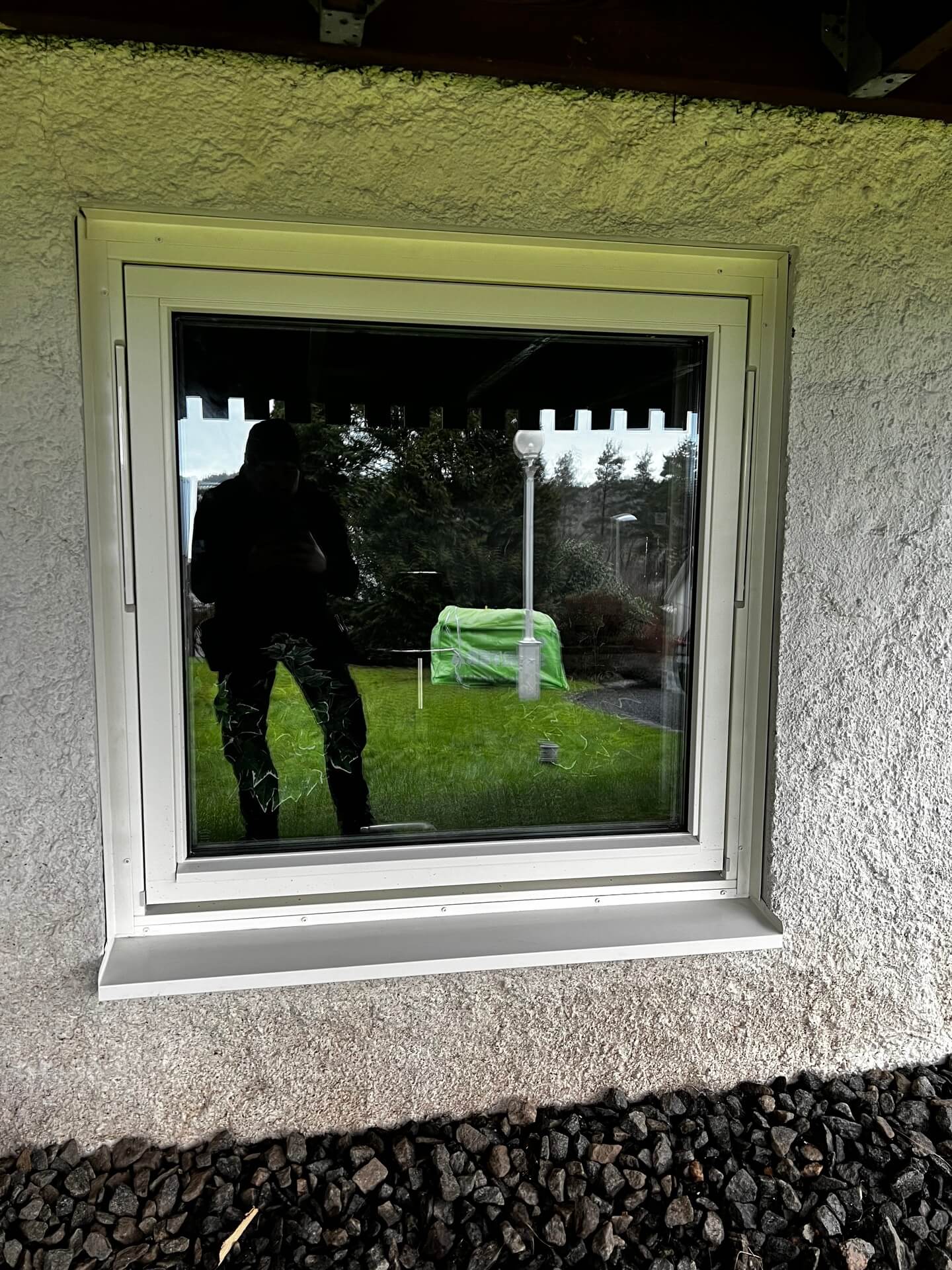Nyinstallerat fönster med vit karm i putsad fasad sett utifrån med trädgårdsutsikt