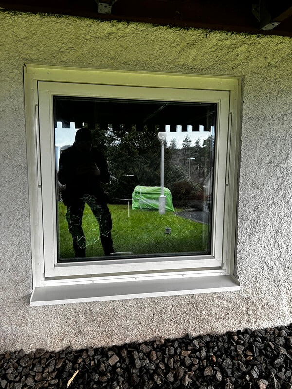 Nyinstallerat fönster med vit karm i putsad fasad sett utifrån med trädgårdsutsikt