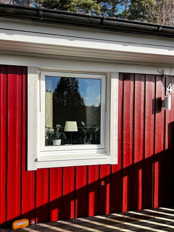 Närbild på nyinstallerat fönster med vit karm på röd träpanelfasad