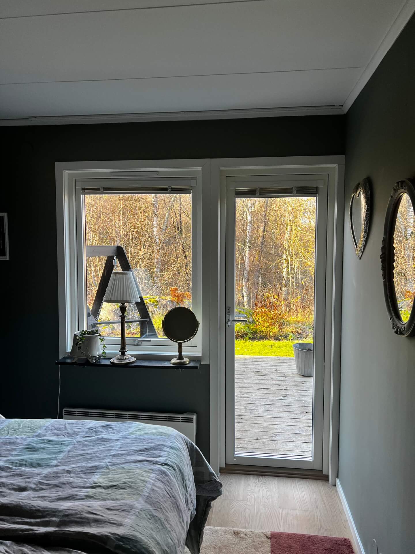 Nyinstallerade fönster med vita karmar och utsikt mot höstträdgård i mörkt sovrum