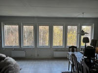 Fem nyinstallerade fönster i rad med vita karmar och utsikt mot lövskog i vardagsrum