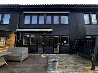 Mörk tvåvåningsvilla med svart träpanelfasad och stora mörka fönsterpartier mot altan
