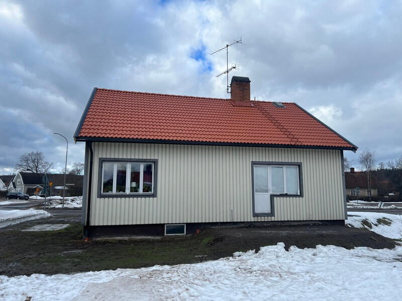 Ljusgrå trävilla med nytt orangerött pannat tak och tegelskorsten en vinterdag med snö