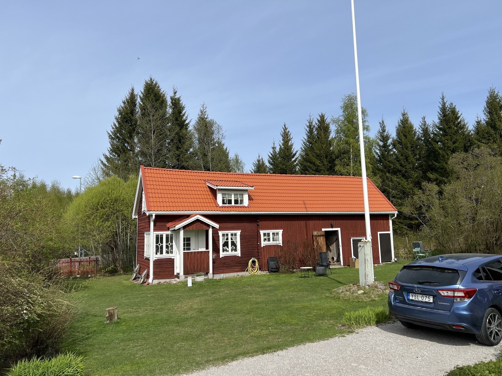 Rödmålat trähus med vita knutar, orangerött pannat tak och frontespis, omgivet av gräsmatta och granar