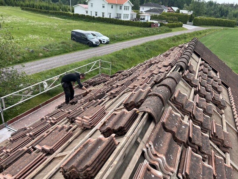 Takläggare river gamla takpannor och staplar dem på taket, med skyddsräcke längs takfoten