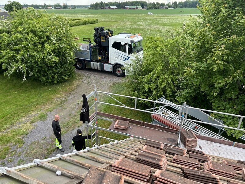Lastbil med kran och byggställning vid ett takbyte, med gamla takpannor staplade på taket