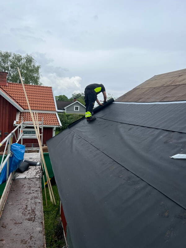 Takläggare rullar ut svart underlagspapp på taket under ett takbyte