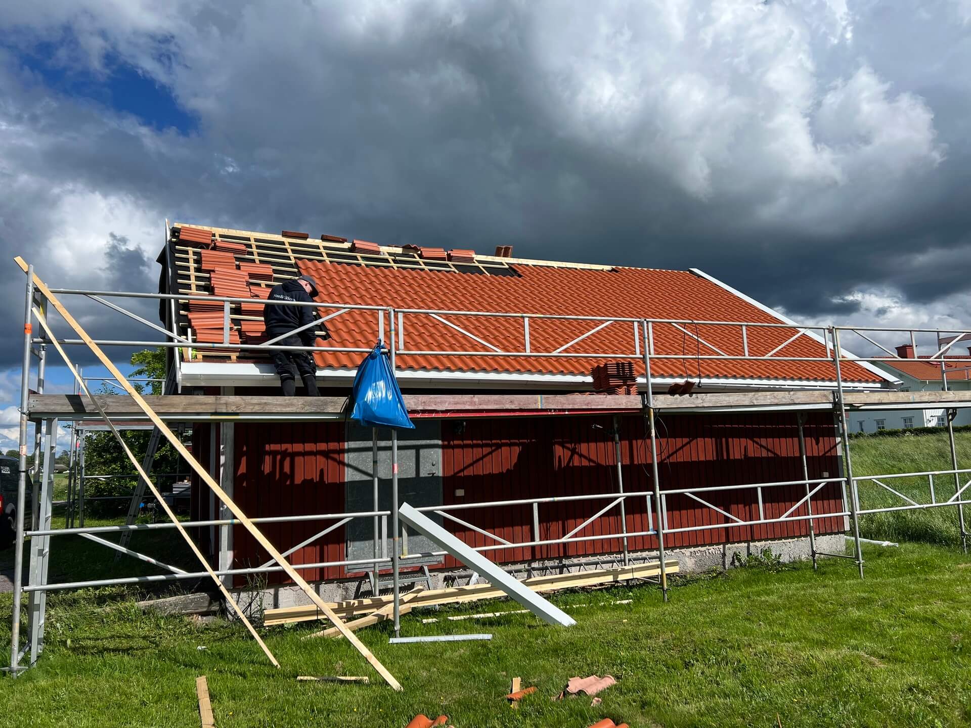 Rödmålat trähus med byggställning runt om medan takläggare tar bort gamla röda takpannor