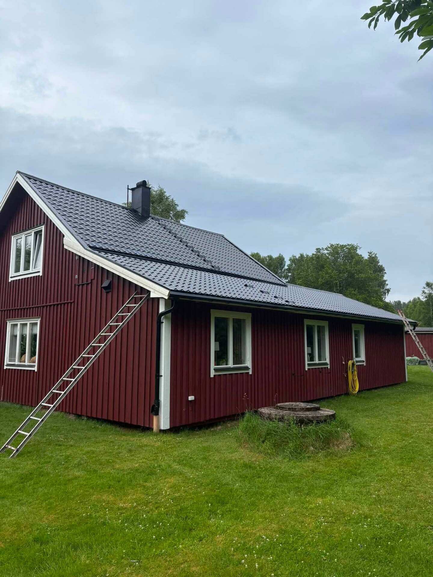 Rödmålad villa i trä med nylagt mörkt plåttak, sedd från långsidan