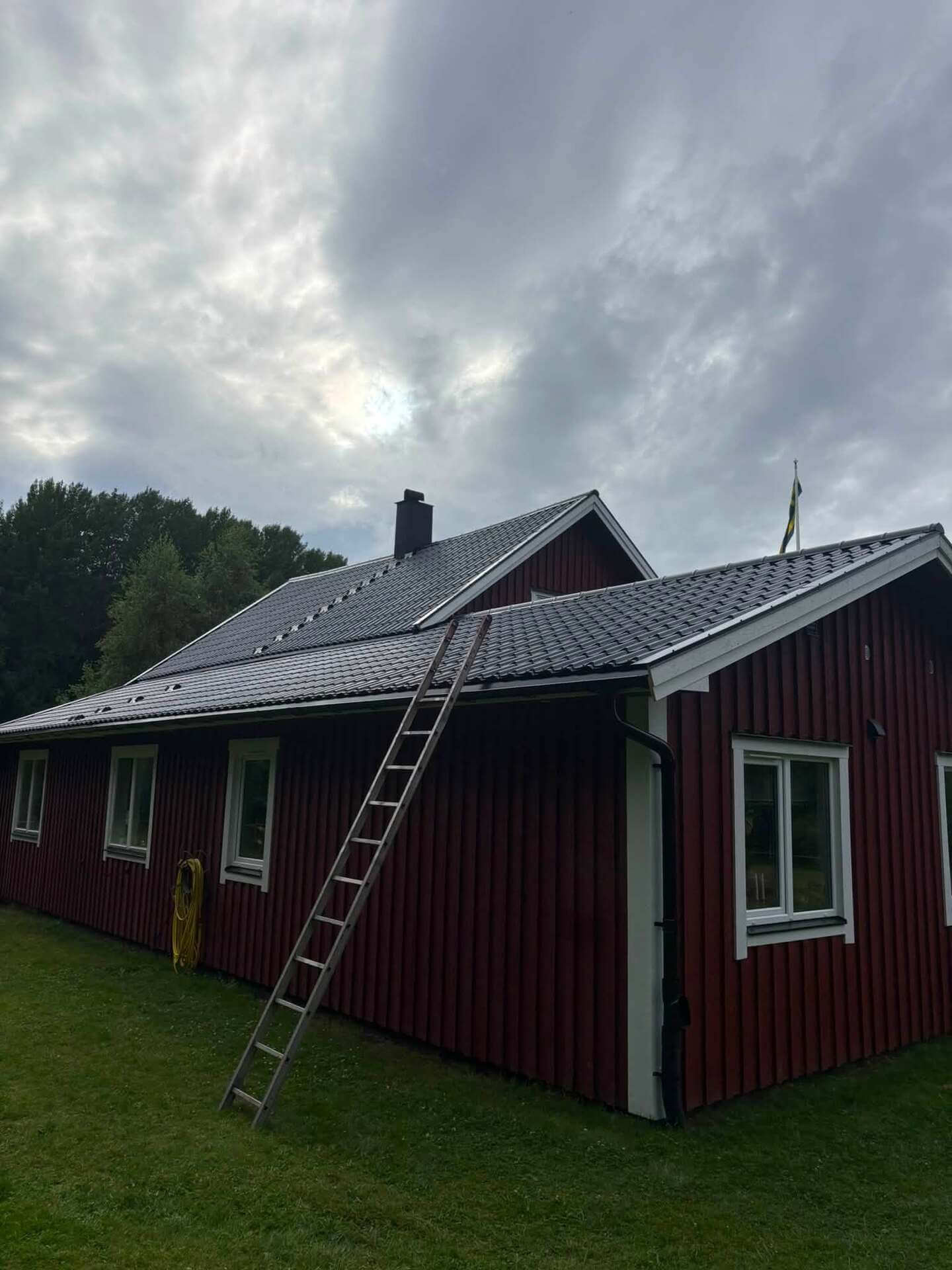Nylagt mörkt plåttak på rödmålad villa, stege uppställd mot takfoten