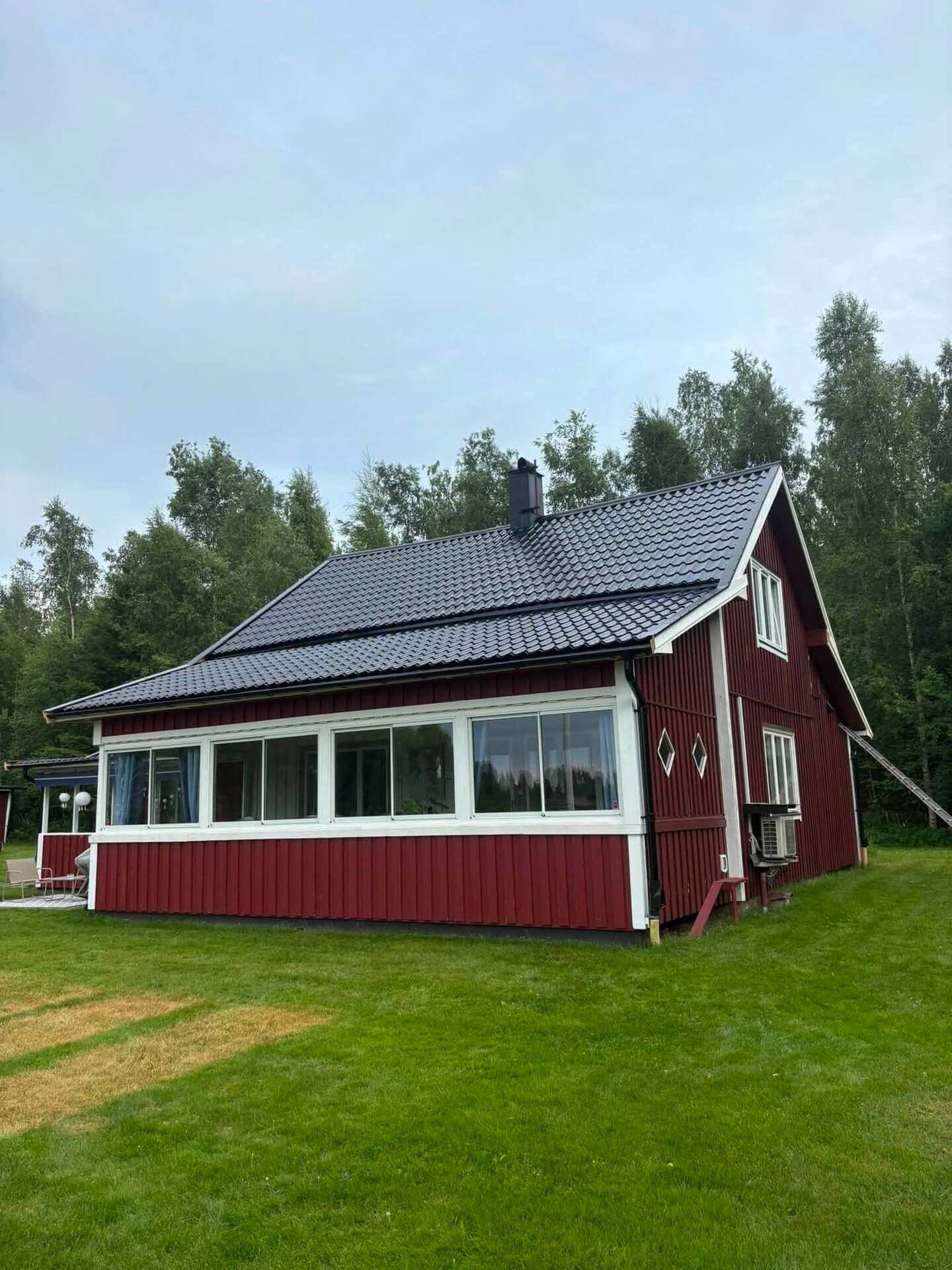 Rödmålad villa med nylagt mörkt plåttak och inglasad veranda med vita fönsterfoder