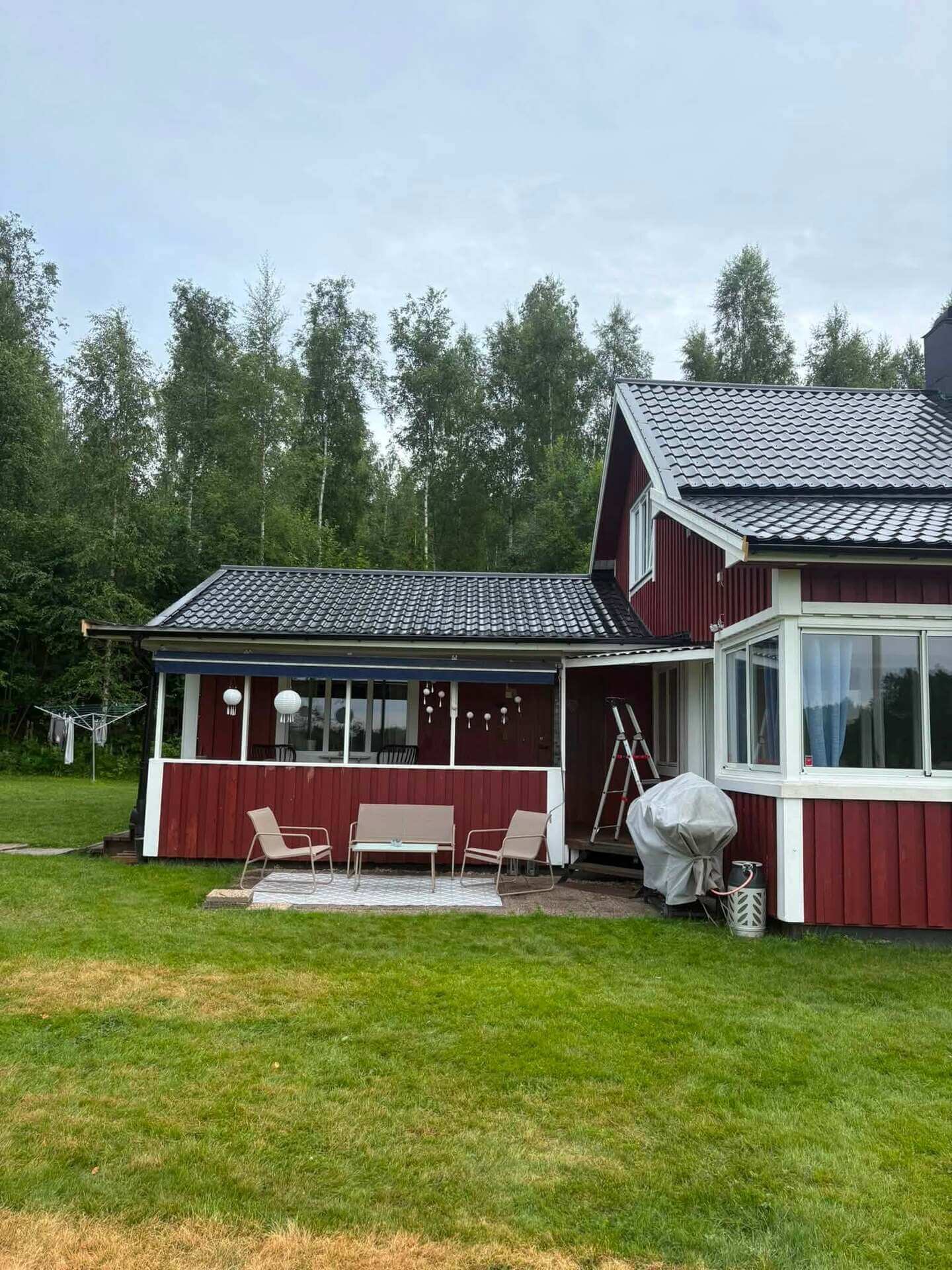 Rödmålad villa med nylagt mörkt tak, altan med tak och uteplats mot gräsmattan