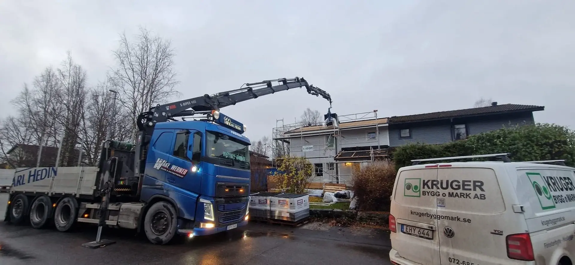 Lastbil med kran lyfter takmaterial till villa under pågående takbyte