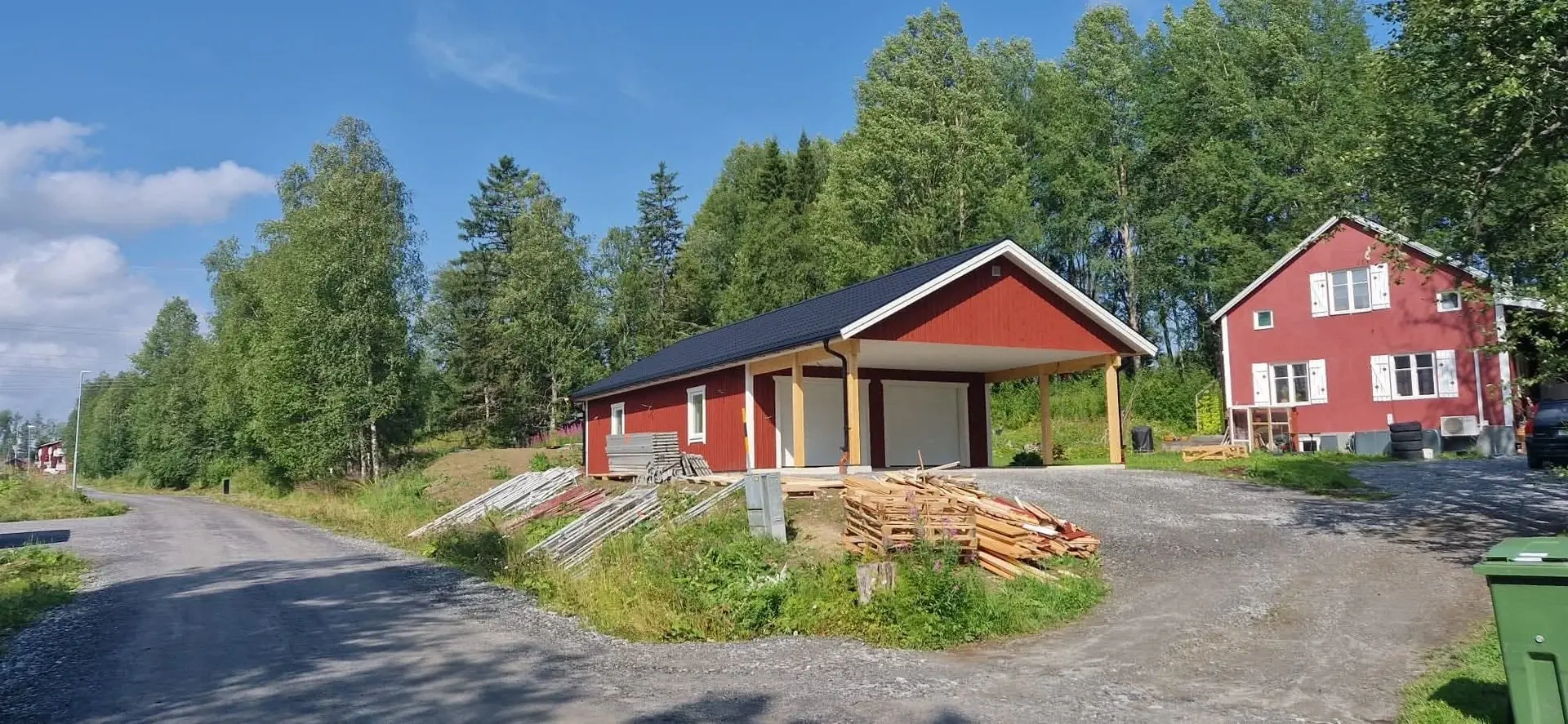 Färdigt rött garage med mörkt tak och öppen carport