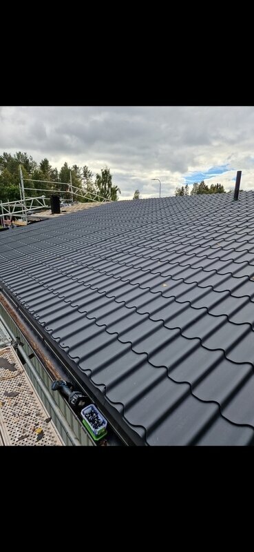 Färdigt mörkgrått betongpannetak på villa med byggnadsställning kvar