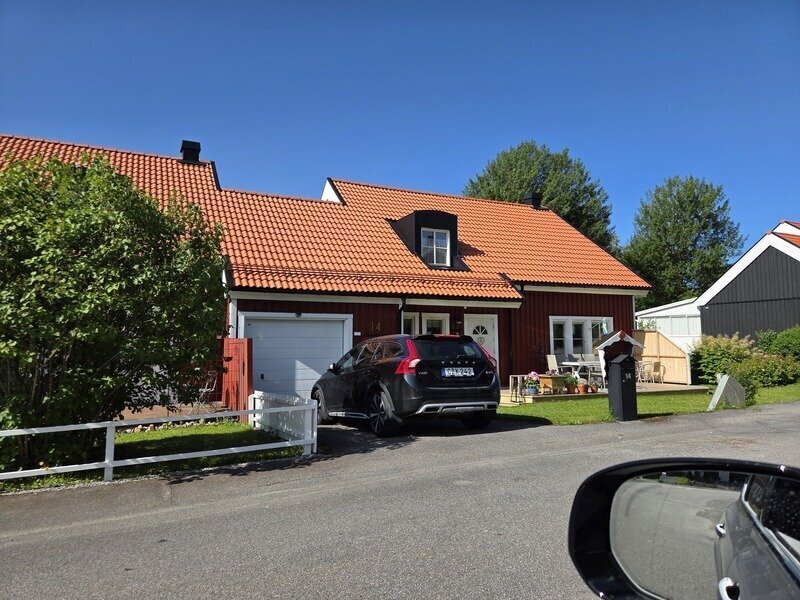 Röd villa med orange tegelpannetak och garage sedd från gatan i sommarmiljö