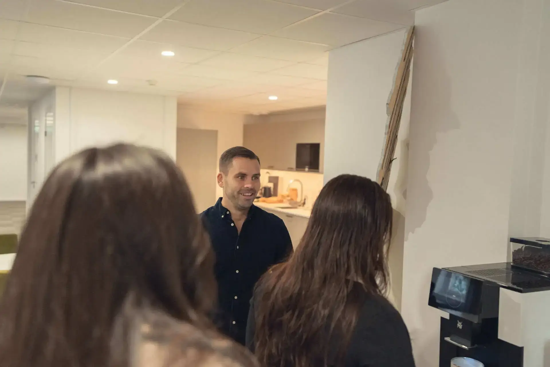Kollegor i samtal i köket, en ler mot kameran