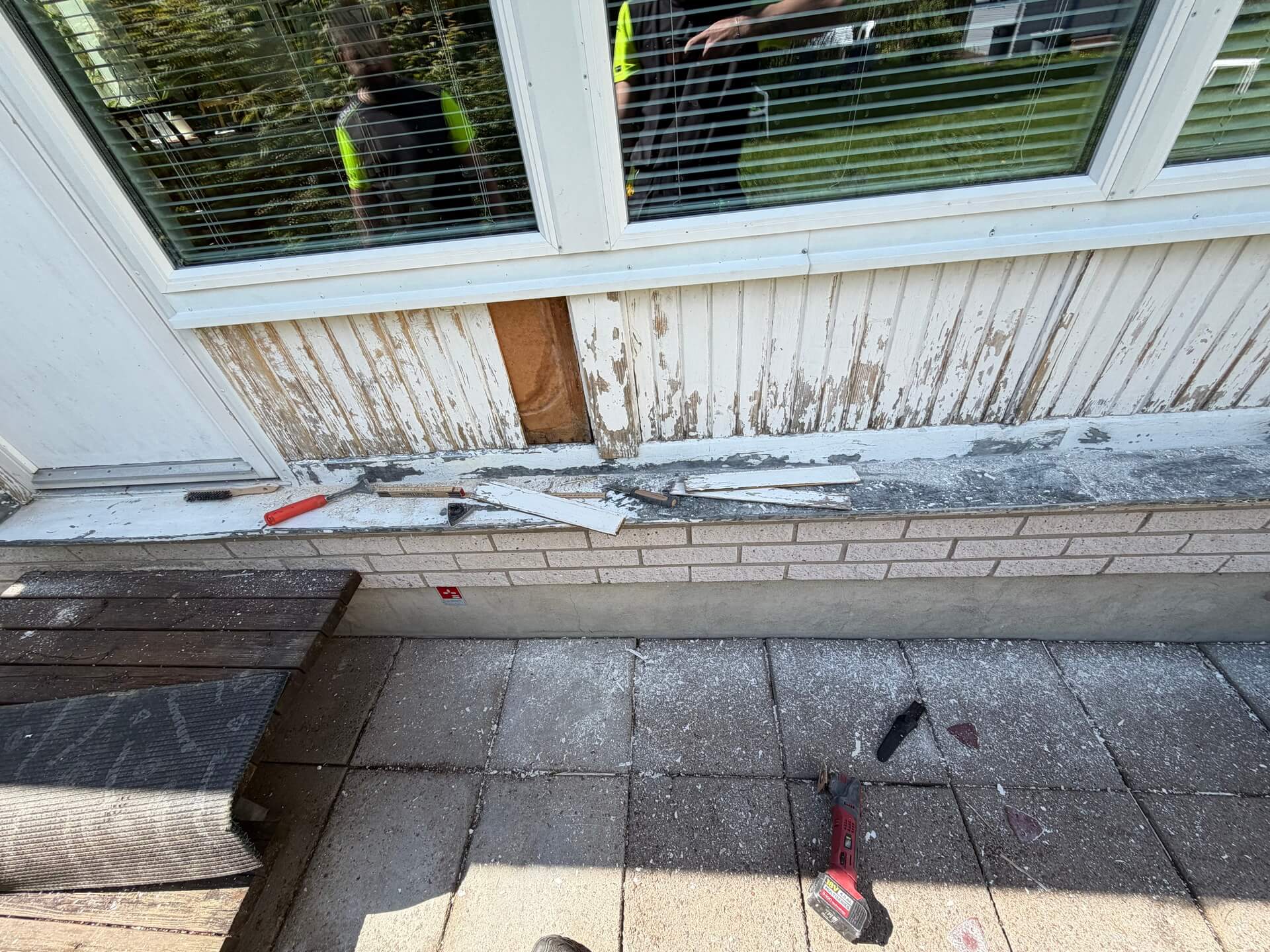 Gammal fasadpanel demonteras under fönster vid fasadrenovering i Stockfallet