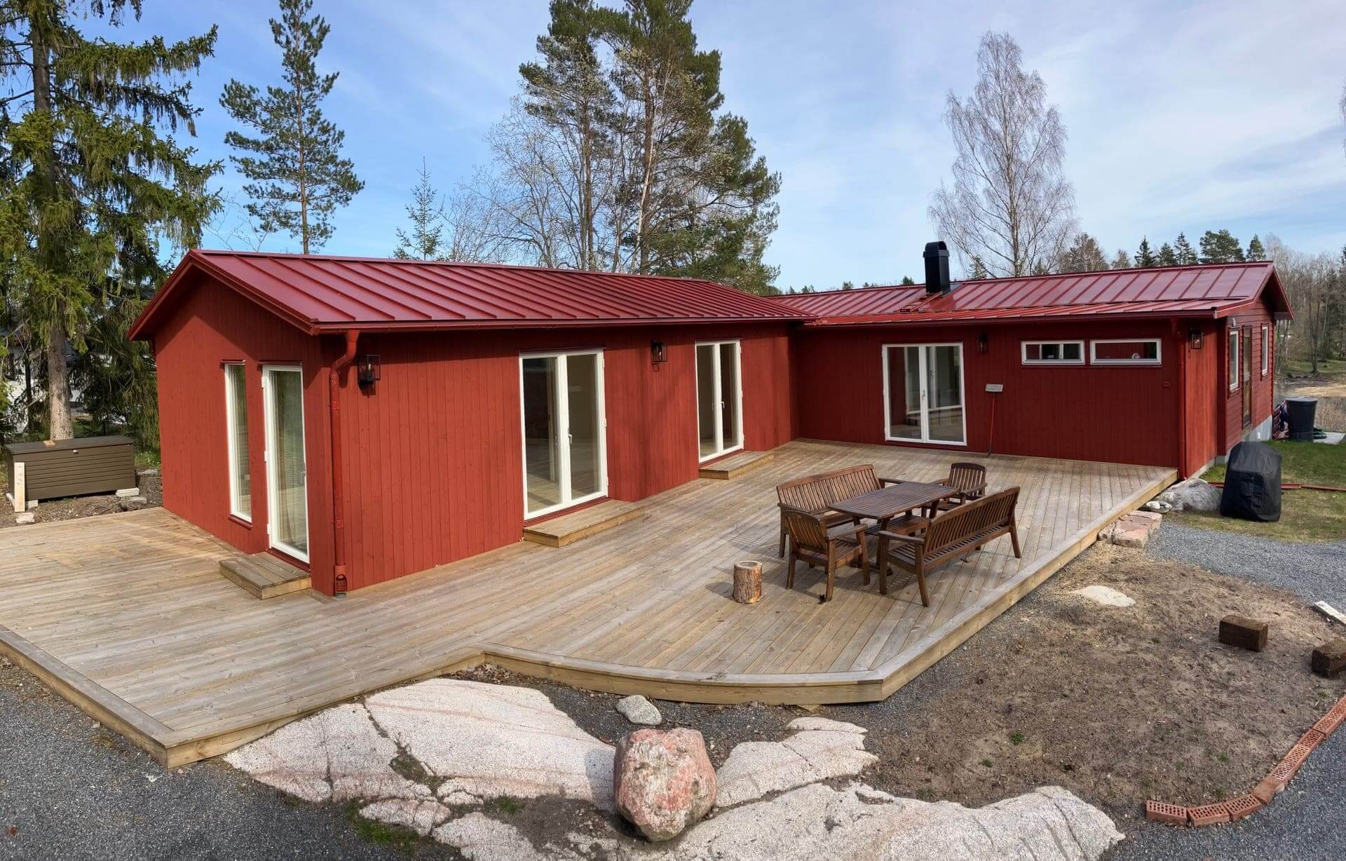 Röd tillbyggnad med plåttak, stora glaspartier och nytt trädäck