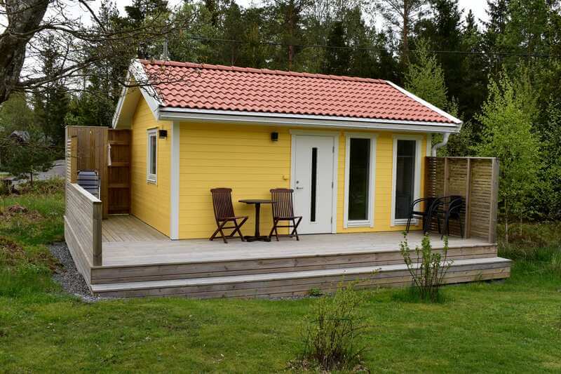 Gult attefallshus med tegelrött tak och altan längs framsidan, byggt av Tunbygg
