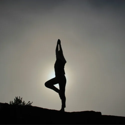 person doing yoga on a hill side siloette