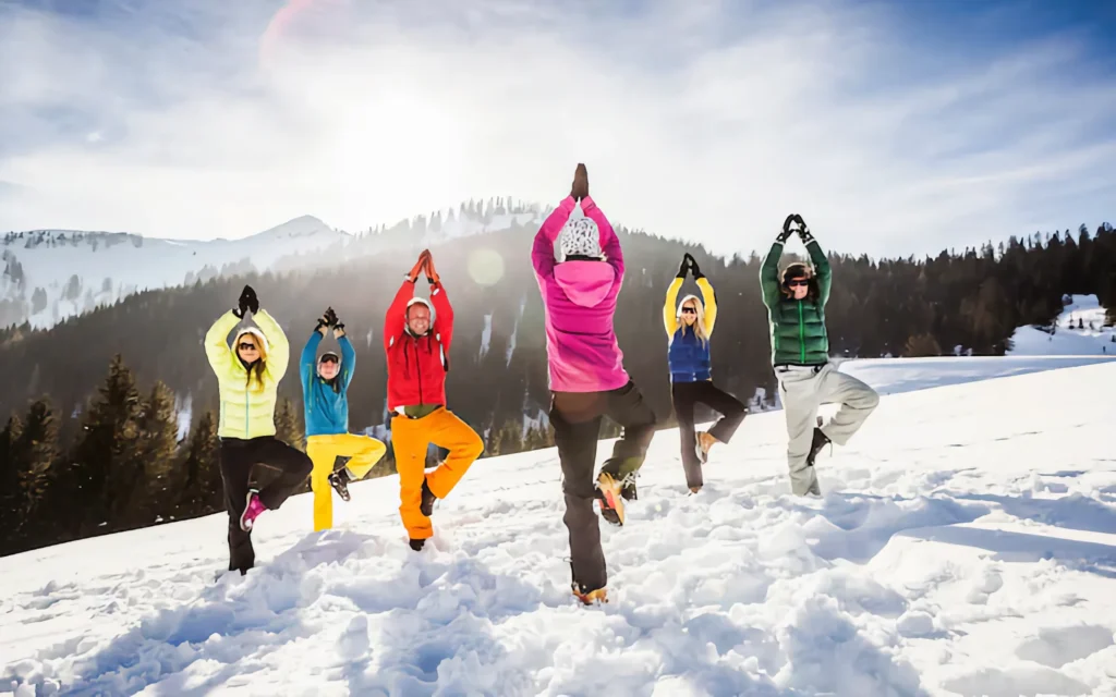 Group of skiers doing the tree pose on a snowy mountain top.
