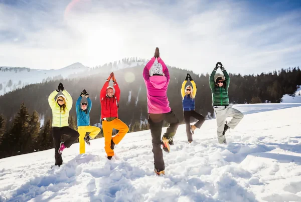 Group of skiers doing the tree pose on a snowy mountain top.