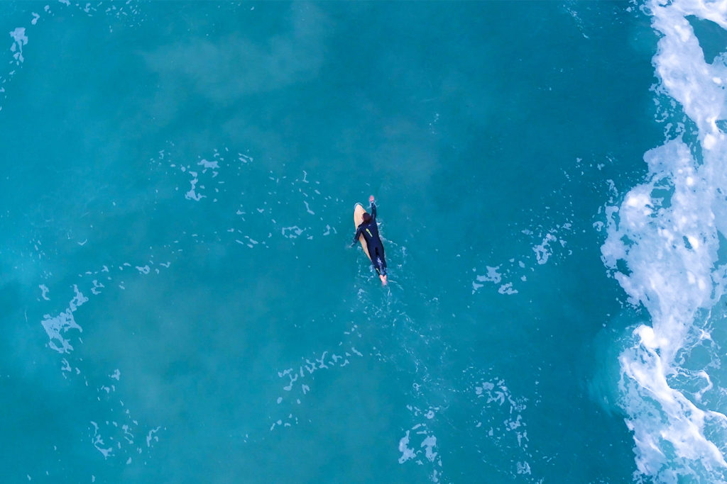 James Otter Alan Stokes in the water surfing a wooden surfboard