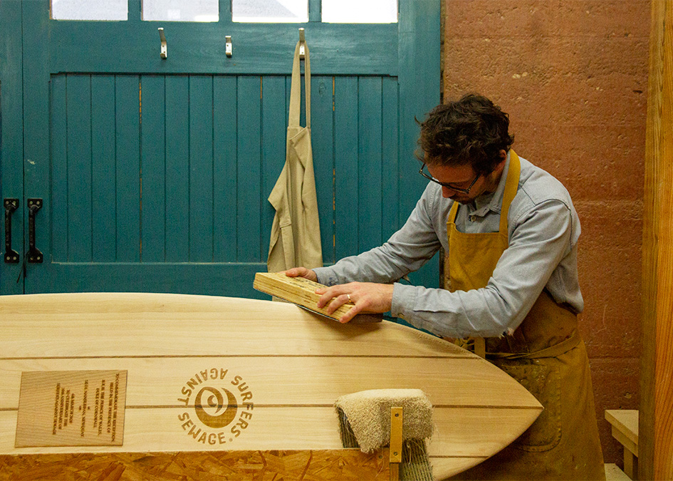prince of wales prince charles duke of cornwall signs wooden surfboard to signify patronage for surfers against sewage hugo tagholm James Otter making surfboard in workshop