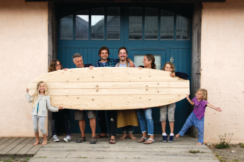 Family with wooden paddleboard outside the otter surfboards workshop with Chris and James
