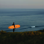 James Otter Seasaw at Perran Sands Wooden Surfboard with surfer on the coast in Cornwall