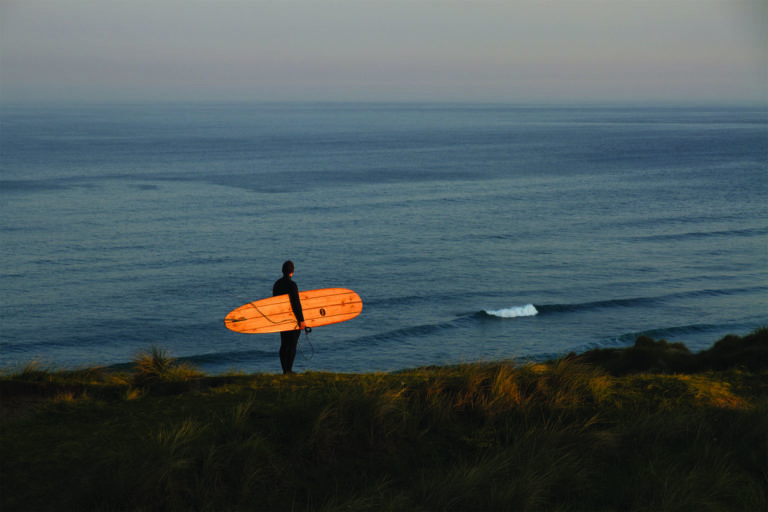 James Otter Seasaw at Perran Sands Wooden Surfboard with surfer on the coast in Cornwall
